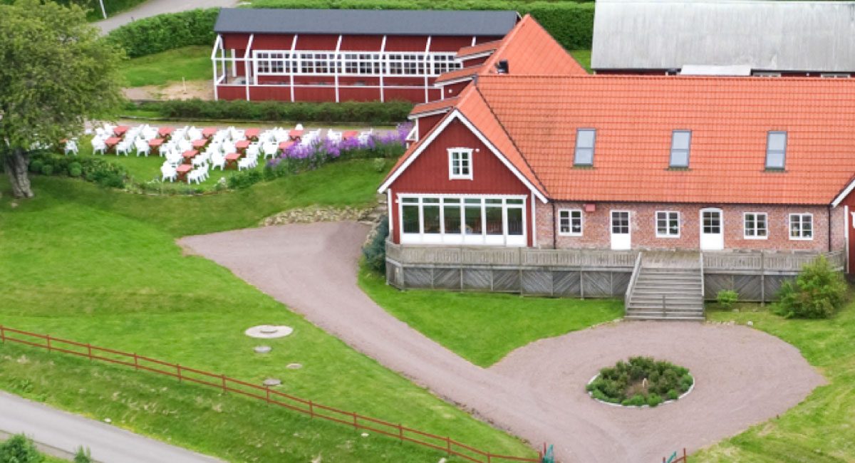 Gården från ovan: röda byggnader med tegeltak, uteservering med vita stolar och grusplan